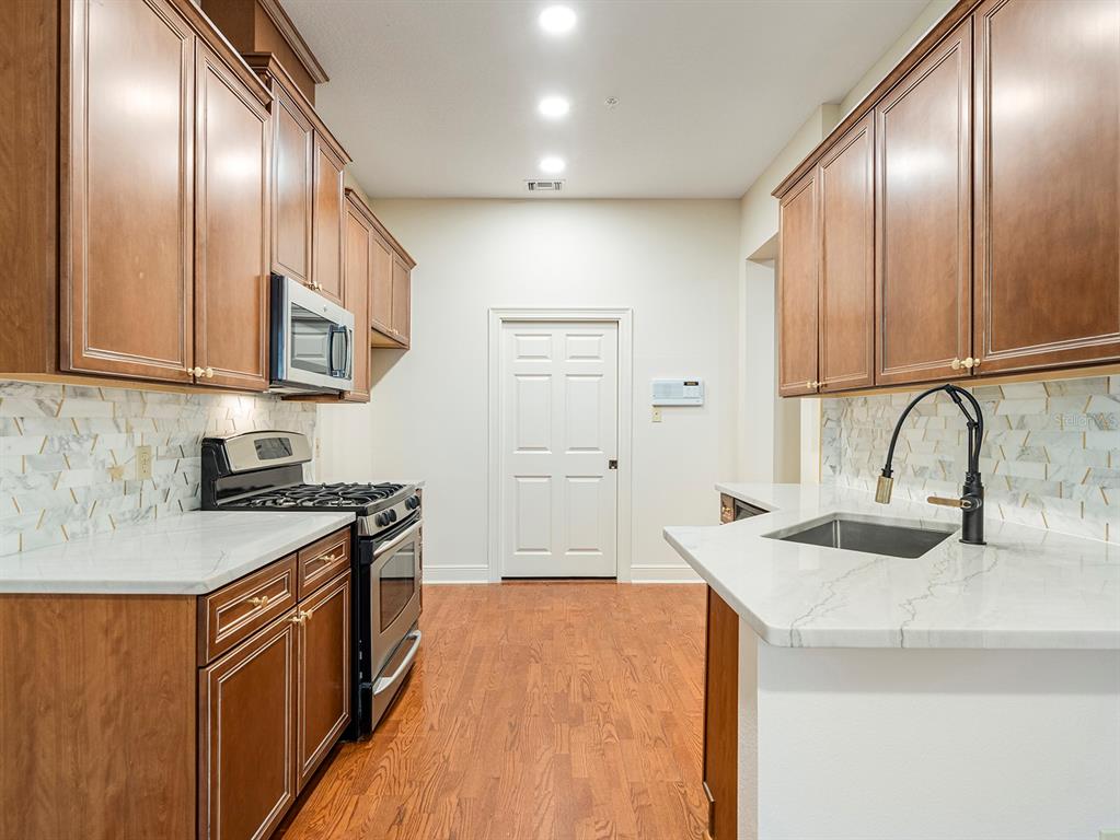A kitchen features wood cabinets, white marble-style countertops, stainless steel appliances, and hardwood flooring — 1223 COUNTRY CLUB OAKS CIRCLE, ORLANDO, FL