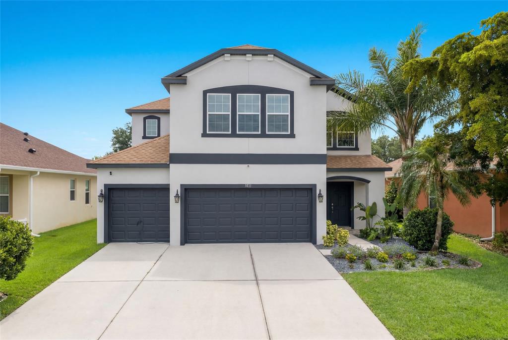 A two-story house with a three-car garage, white stucco walls, and dark gray trim — 5815 ARBOR WOOD COURT, BRADENTON, FL