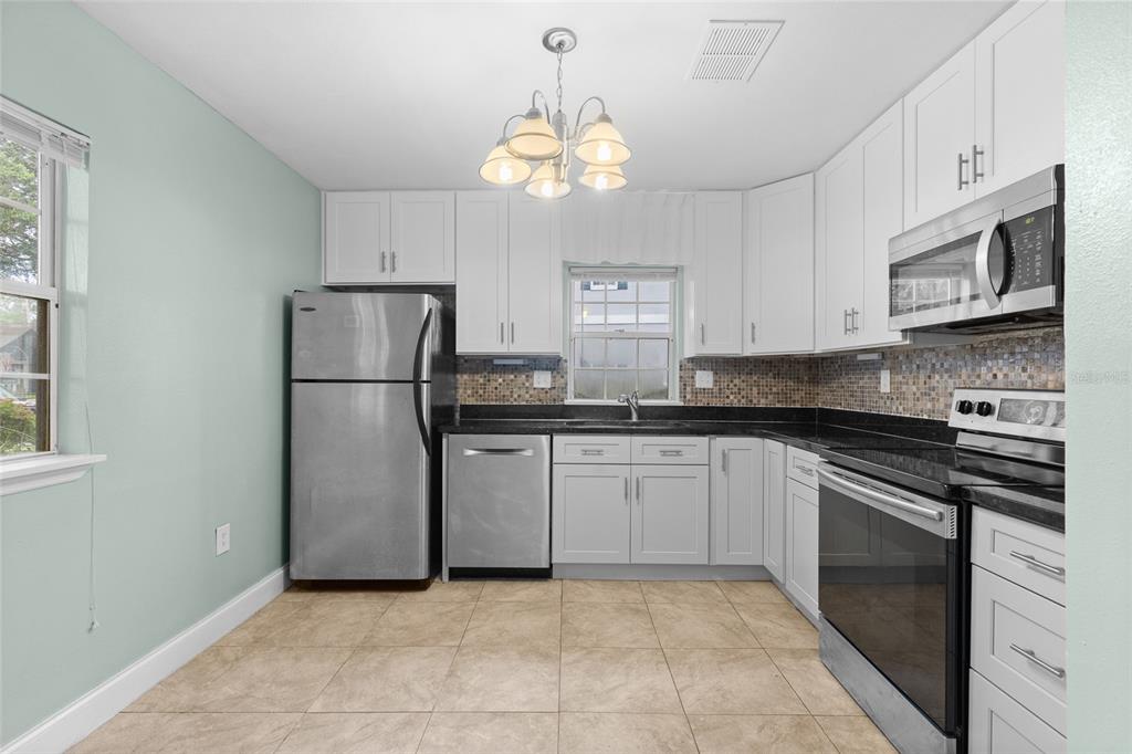 A kitchen features white cabinets, black countertops, stainless steel appliances, and light-colored tile flooring — 3116 CLUBSIDE DRIVE, LONGWOOD, FL
