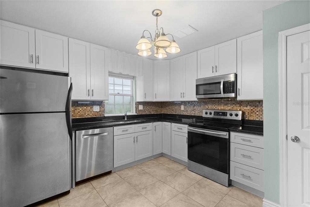 A kitchen with white cabinets, stainless steel appliances, black countertops, and a tile backsplash — 3116 CLUBSIDE DRIVE, LONGWOOD, FL