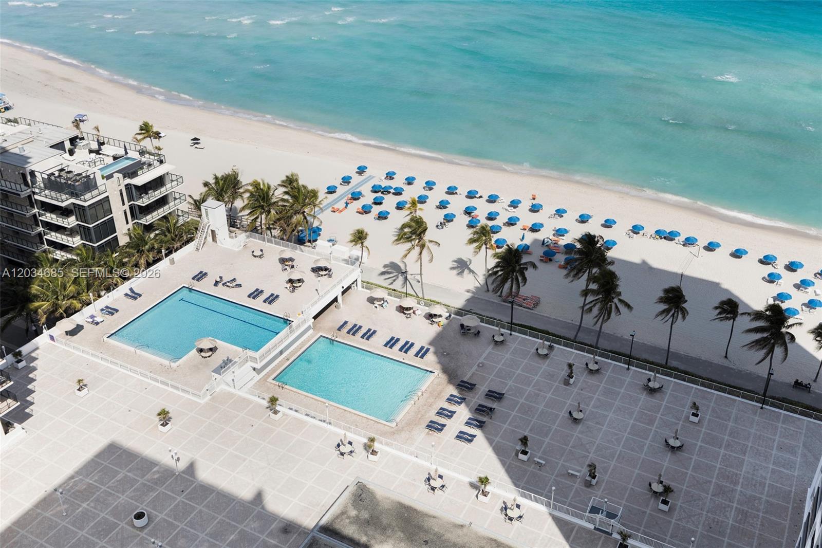 An aerial view shows two swimming pools on a tiled deck beside a sandy beach — 2401 S Ocean Dr # 2402, Hollywood FL 33019, HOLLYWOOD, FL
