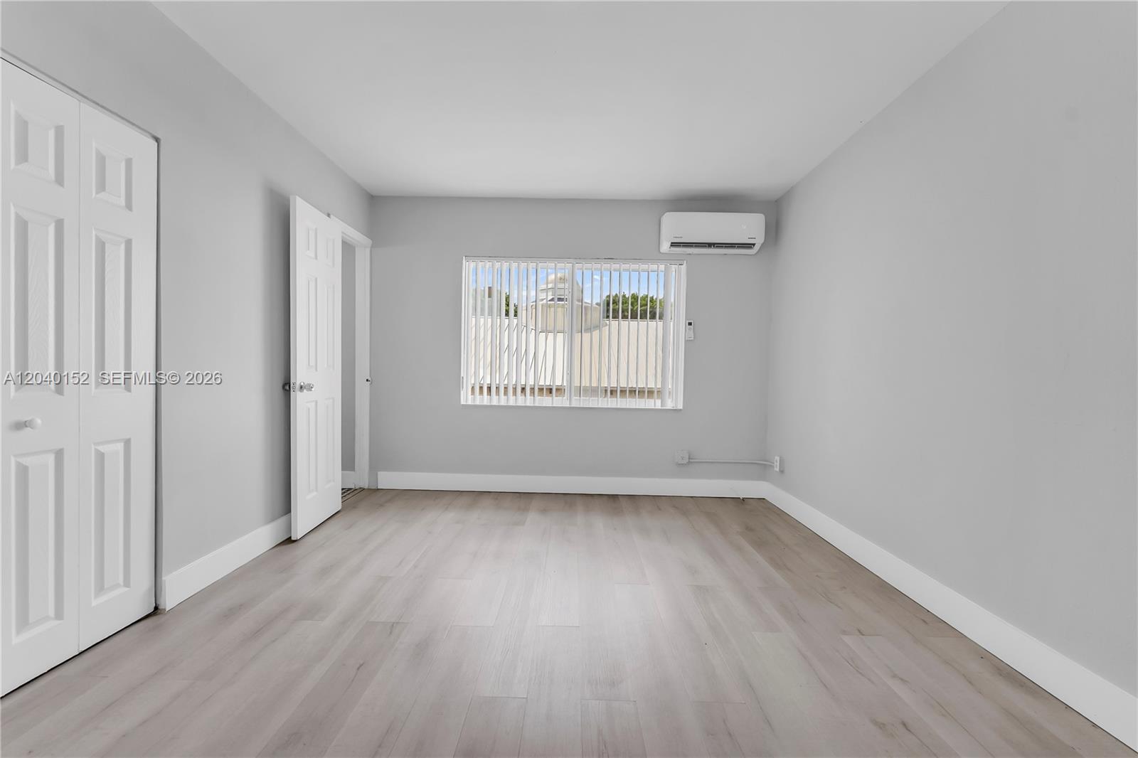 An empty bedroom features light gray walls, wood-look flooring, a window with blinds, and an AC unit — 6647 SW 59th Pl # 202, South Miami FL 33143, SOUTH MIAMI, FL