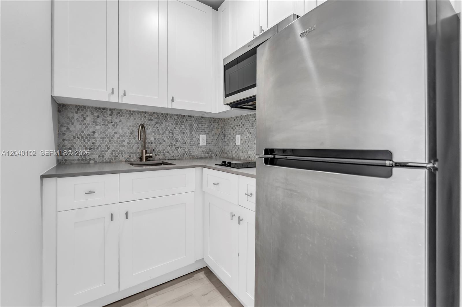 A small kitchen features white cabinets, a stainless steel refrigerator, and a gray hexagonal backsplash — 6647 SW 59th Pl # 202, South Miami FL 33143, SOUTH MIAMI, FL