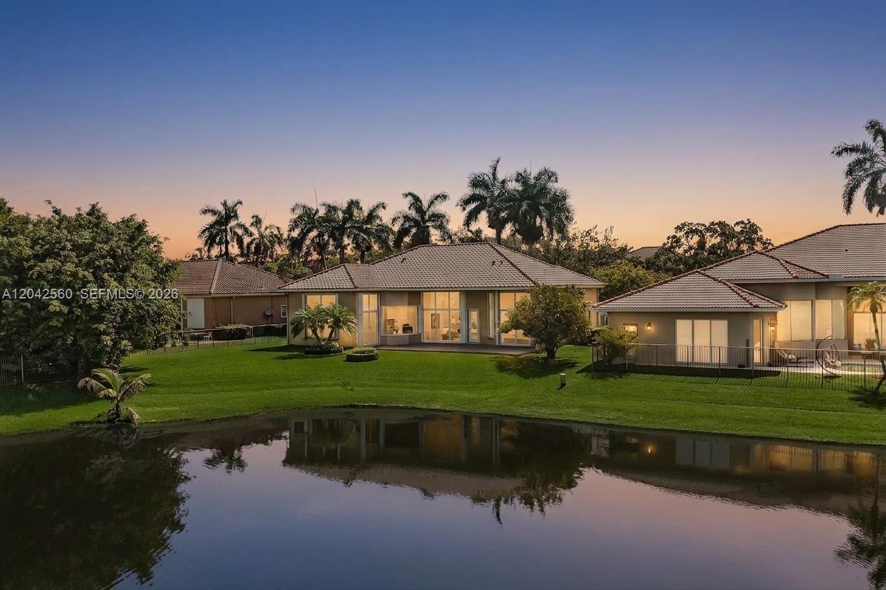 A view of the rear exterior of a house overlooking a lake at sunset — 2733 Meadowood Dr, Weston FL 33332, WESTON, FL