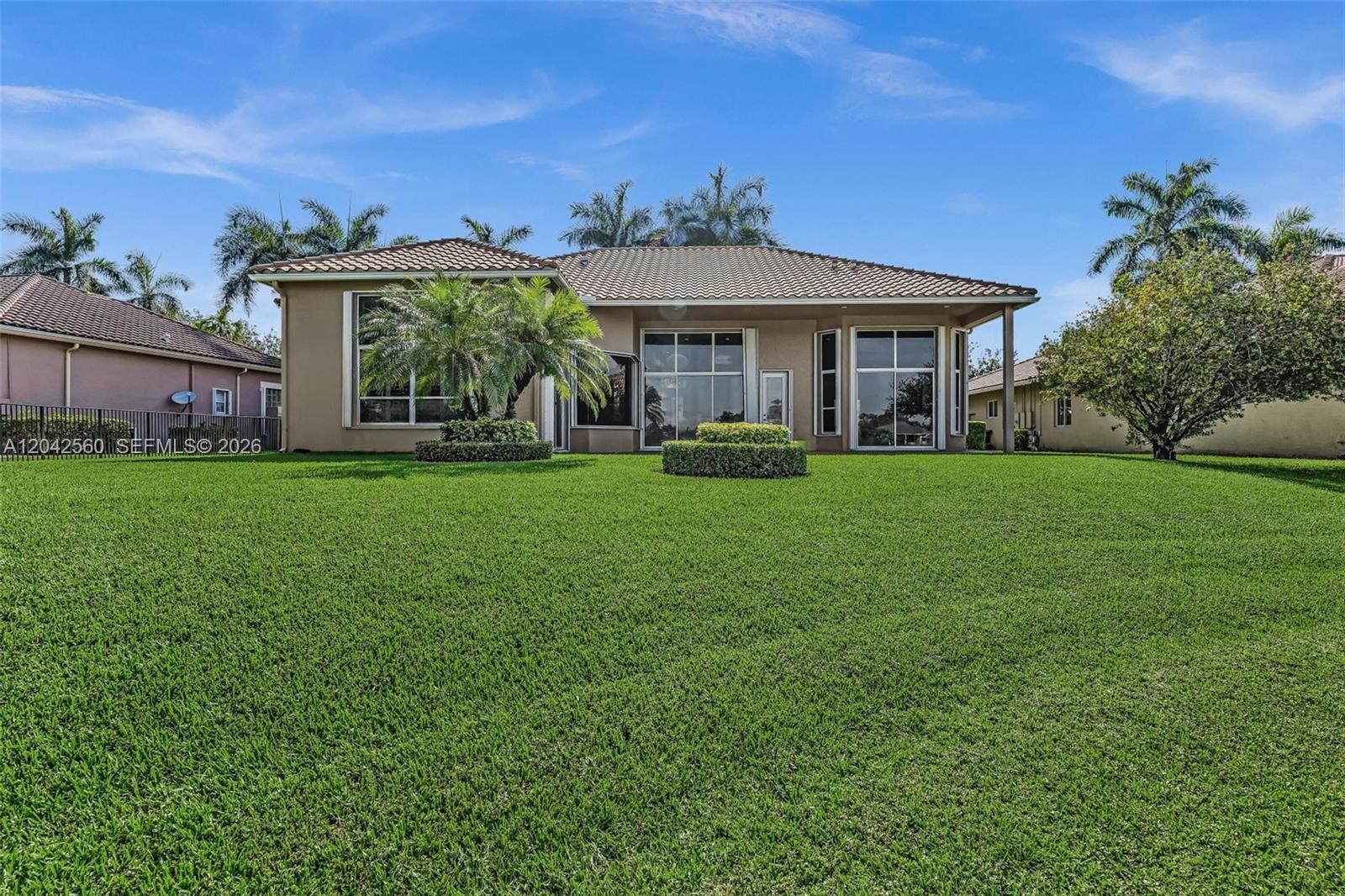 The rear exterior of a single-story house features a large lawn and palm trees — 2733 Meadowood Dr, Weston FL 33332, WESTON, FL