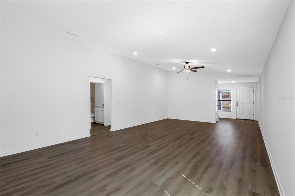 An empty living room features white walls, recessed lighting, a ceiling fan, and wood-look flooring — 620 BLACKTHORN DRIVE, LAKELAND, FL