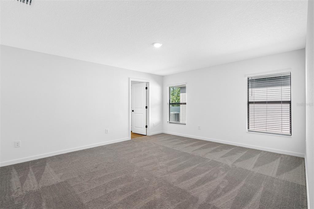 An empty bedroom features gray carpet, white walls, two windows, and a doorway — 620 BLACKTHORN DRIVE, LAKELAND, FL