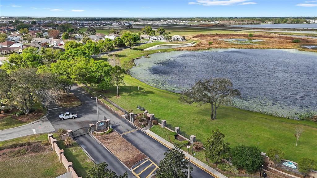 An aerial view shows a gated community entrance with a lake and surrounding residential homes — 496 TERRANOVA STREET, WINTER HAVEN, FL