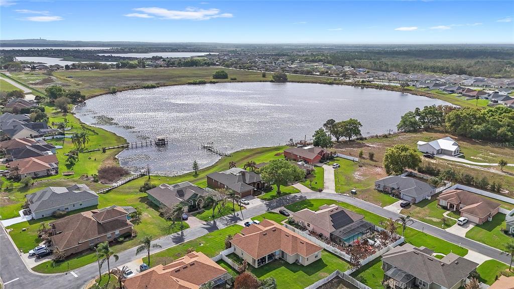 An aerial view shows suburban houses surrounding a large lake with a wooden pier — 496 TERRANOVA STREET, WINTER HAVEN, FL
