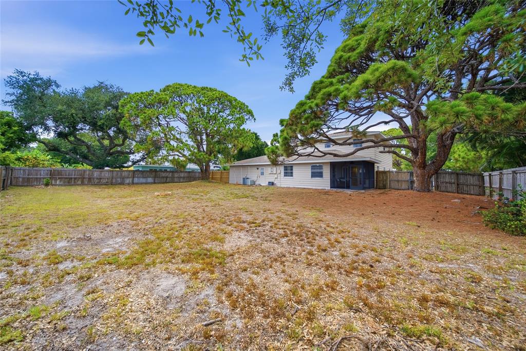 A large, grassy backyard features mature pine trees and a beige house with a screened porch — 5315 9TH AVENUE DRIVE W, BRADENTON, FL