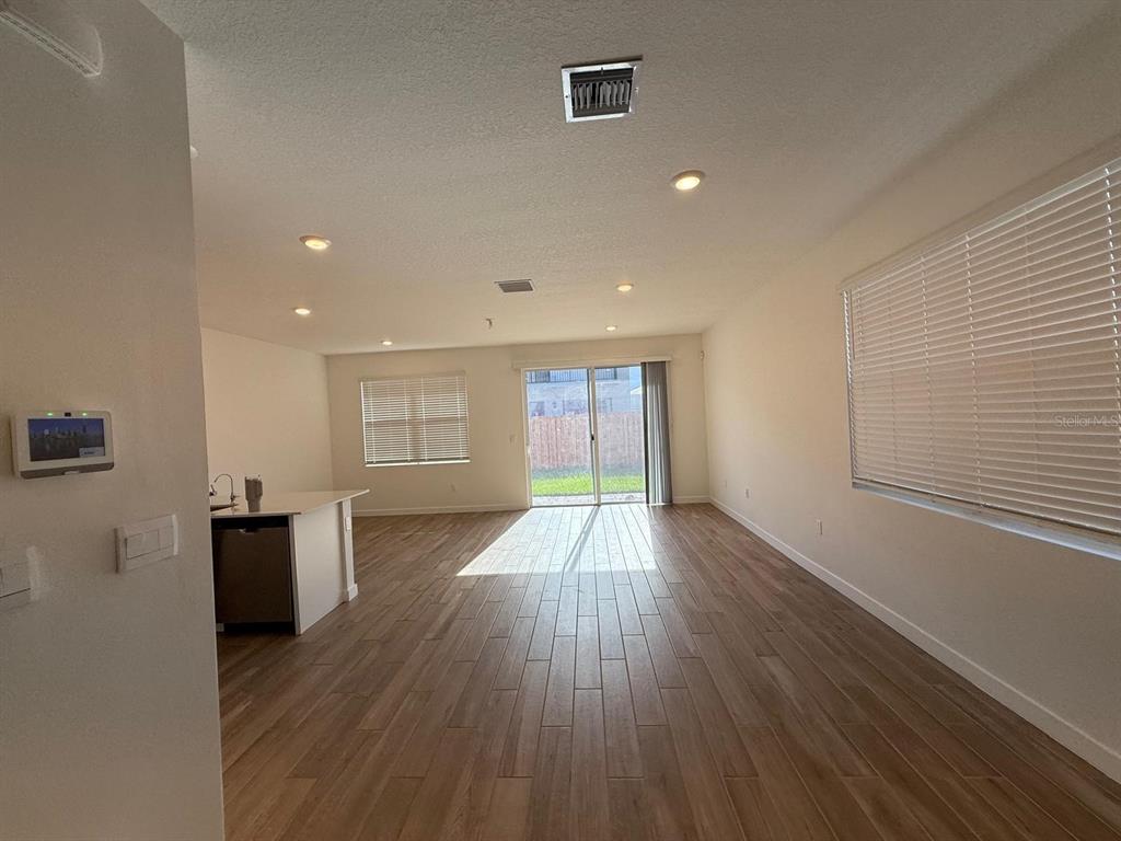 An open-concept living area features light wood-look flooring, recessed lighting, and a sliding glass door — 142 NE 14TH TERRACE, HOMESTEAD, FL