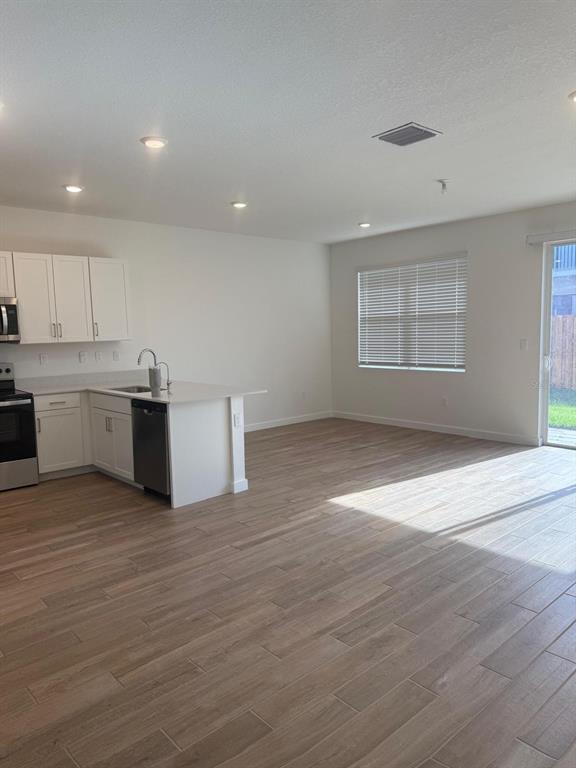 An open-concept kitchen with white cabinets and wood-look tile flooring leads to a living area — 142 NE 14TH TERRACE, HOMESTEAD, FL