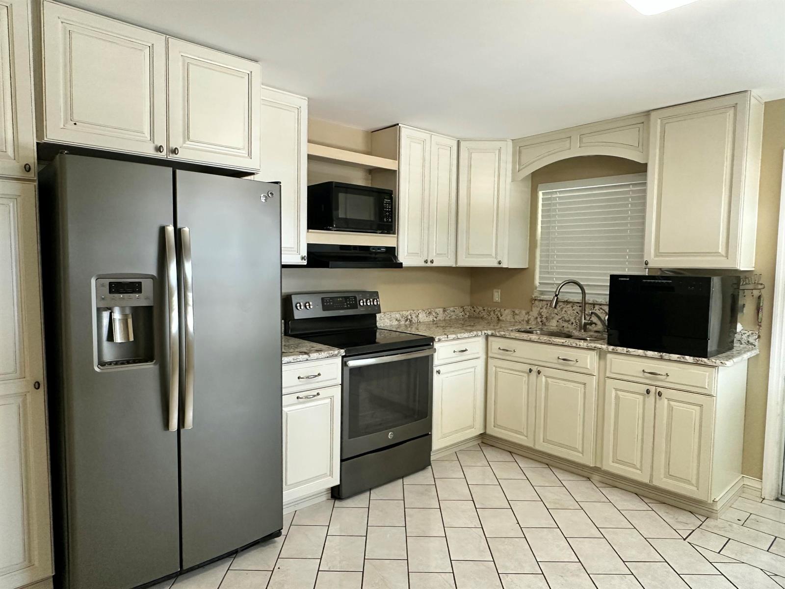 A kitchen features off-white cabinets, stainless steel appliances, granite countertops, and light-colored tile flooring — 1005 NW 5th Street, Okeechobee FL 34972, OKEECHOBEE, FL