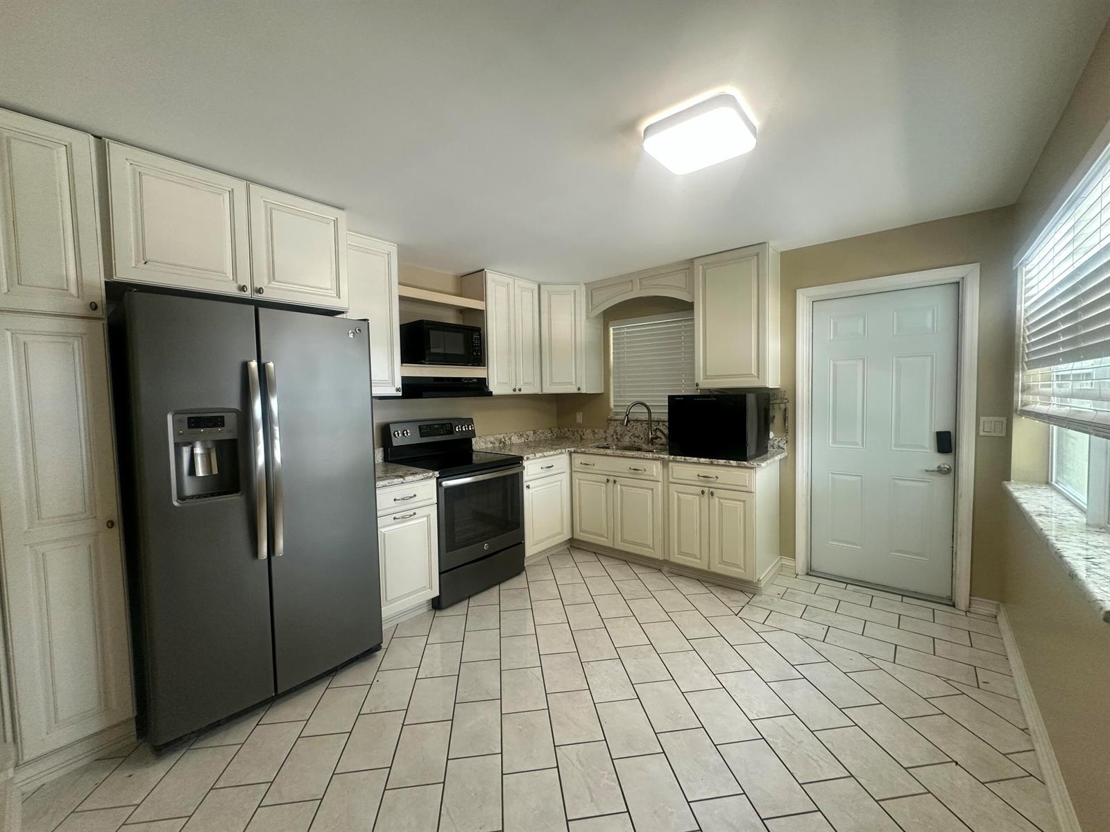 A kitchen features white cabinets, granite countertops, stainless steel appliances, and light-colored tile flooring — 1005 NW 5th Street, Okeechobee FL 34972, OKEECHOBEE, FL