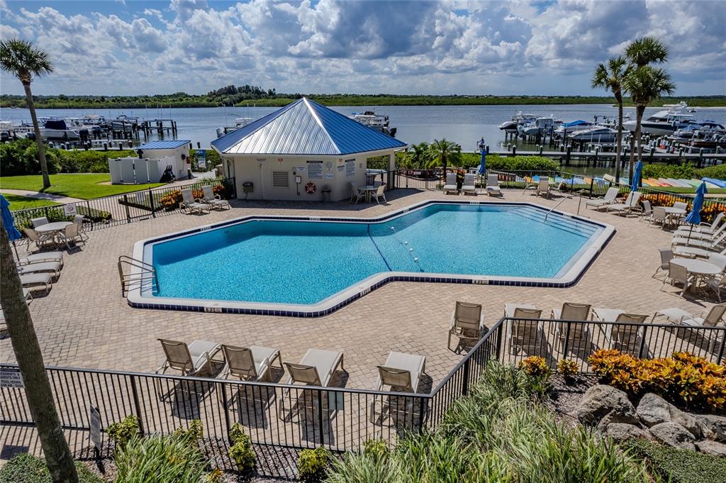 An outdoor swimming pool with lounge chairs sits beside a building overlooking a boat marina — 2700 N PENINSULA AVENUE UNIT 516, NEW SMYRNA BEACH, FL
