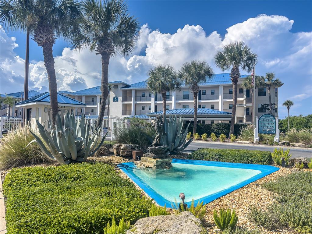 A multi-story apartment building features a blue roof, palm trees, and a front fountain — 2700 N PENINSULA AVENUE UNIT 516, NEW SMYRNA BEACH, FL