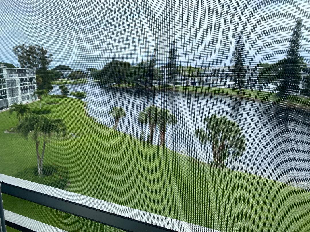 A view of a lake, green lawn, and apartment buildings seen through a window screen — 4096 Westbury H # 4096, Deerfield Beach FL 33442, DEERFIELD BEACH, FL