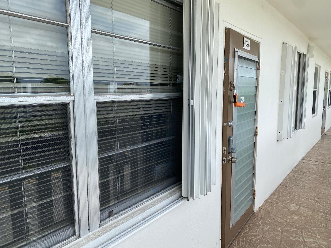 An exterior view of a building hallway showing a louvered door and window with shutters — 4096 Westbury H # 4096, Deerfield Beach FL 33442, DEERFIELD BEACH, FL