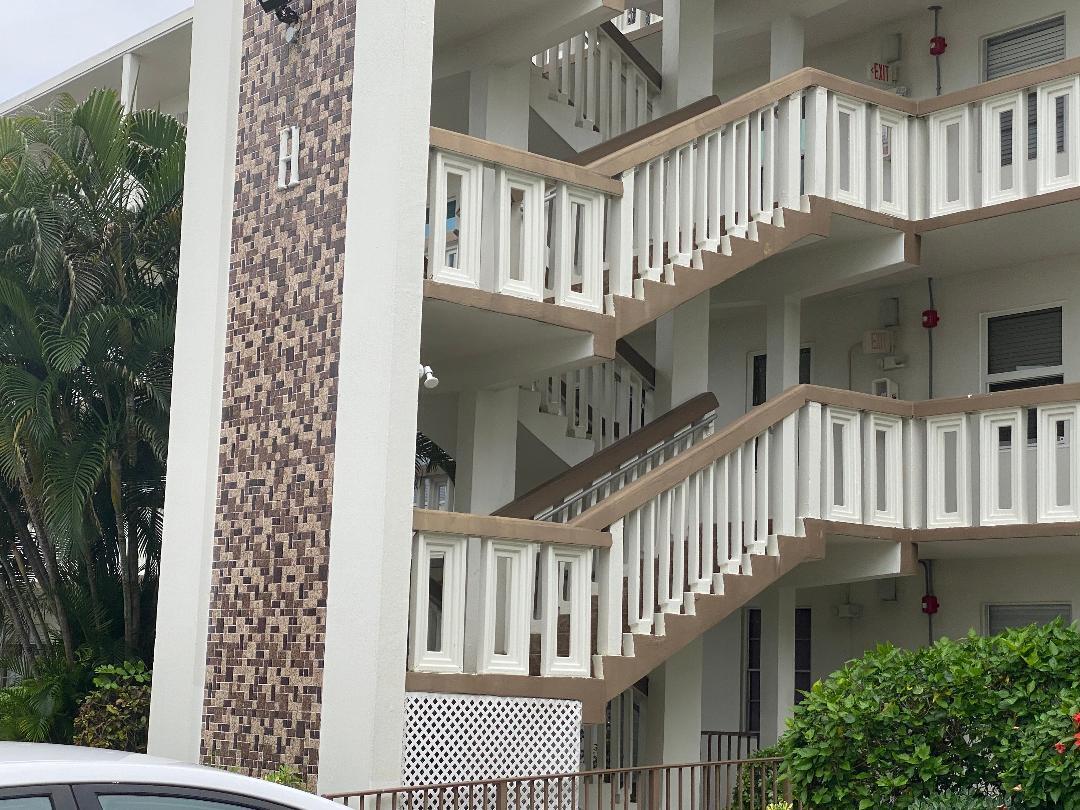 An exterior view of a multi-story apartment building featuring white railings and a tiled pillar — 4096 Westbury H # 4096, Deerfield Beach FL 33442, DEERFIELD BEACH, FL