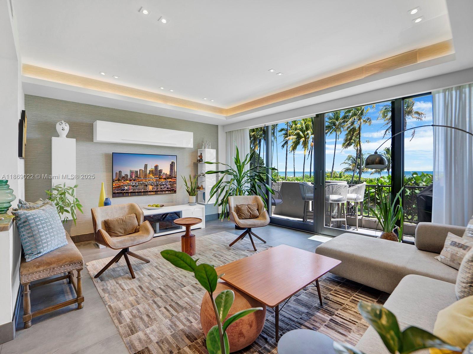 A modern living room features a large television, neutral furniture, and floor-to-ceiling windows overlooking palm trees — 201 Crandon Blvd # 176, Key Biscayne FL 33149, KEY BISCAYNE, FL