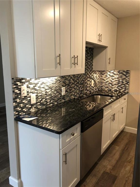 A kitchen features white cabinets, dark granite countertops, a stainless steel sink, and mosaic backsplash — 520 70TH STREET N UNIT 2, ST PETERSBURG, FL