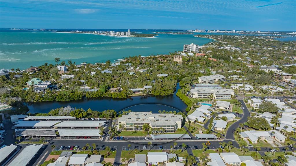 An aerial view shows a multi-story apartment building situated next to a lake and coastline — 101 WHISPERING SANDS DRIVE UNIT 107, SARASOTA, FL
