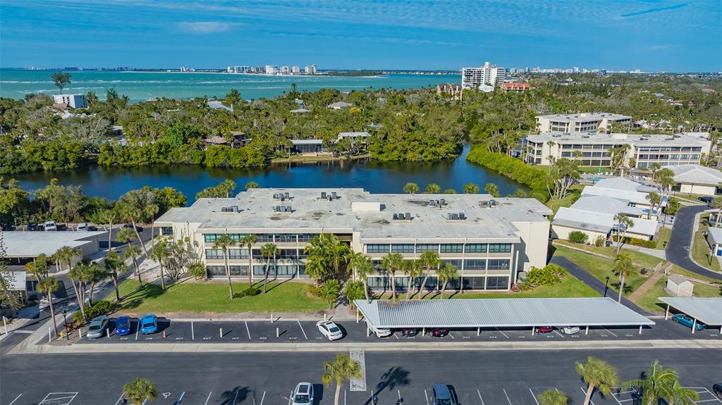 An aerial view shows a multi-story apartment building with a parking lot and covered carports — 101 WHISPERING SANDS DRIVE UNIT 107, SARASOTA, FL