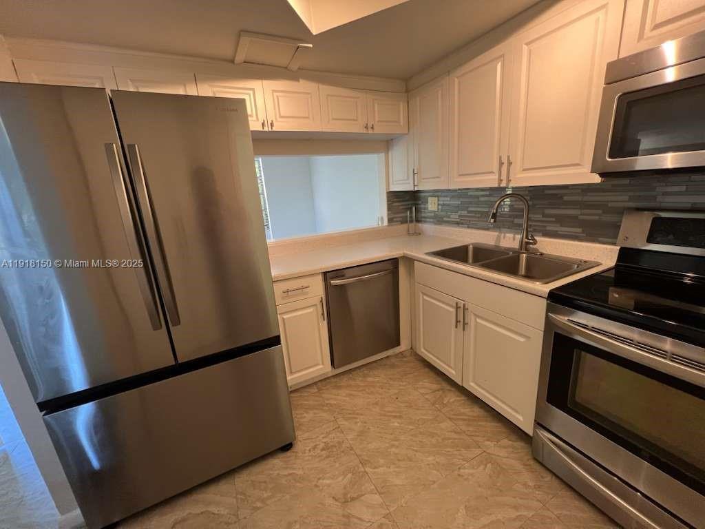 A kitchen features white cabinets, stainless steel appliances, a tiled backsplash, and light-colored flooring — 721 SE 1st Way # B18, Deerfield Beach FL 33441, DEERFIELD BEACH, FL
