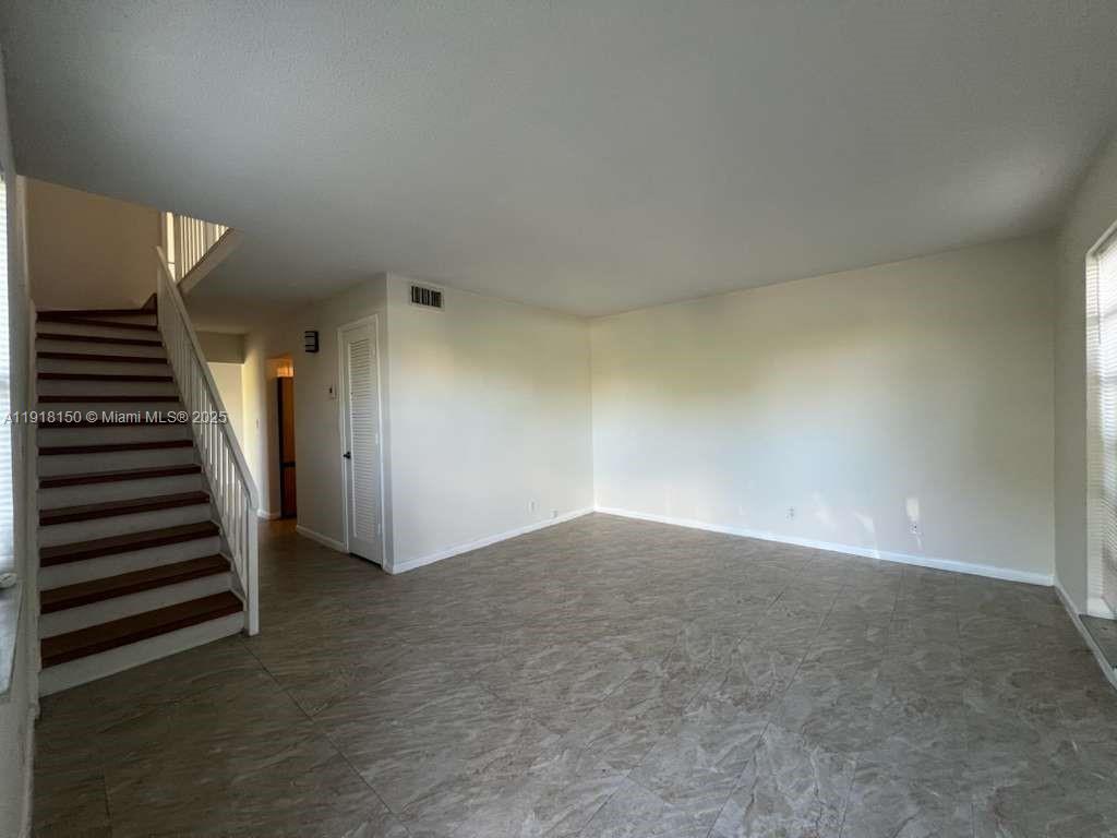 An empty living room features light-colored tile flooring, white walls, and a wooden staircase — 721 SE 1st Way # B18, Deerfield Beach FL 33441, DEERFIELD BEACH, FL
