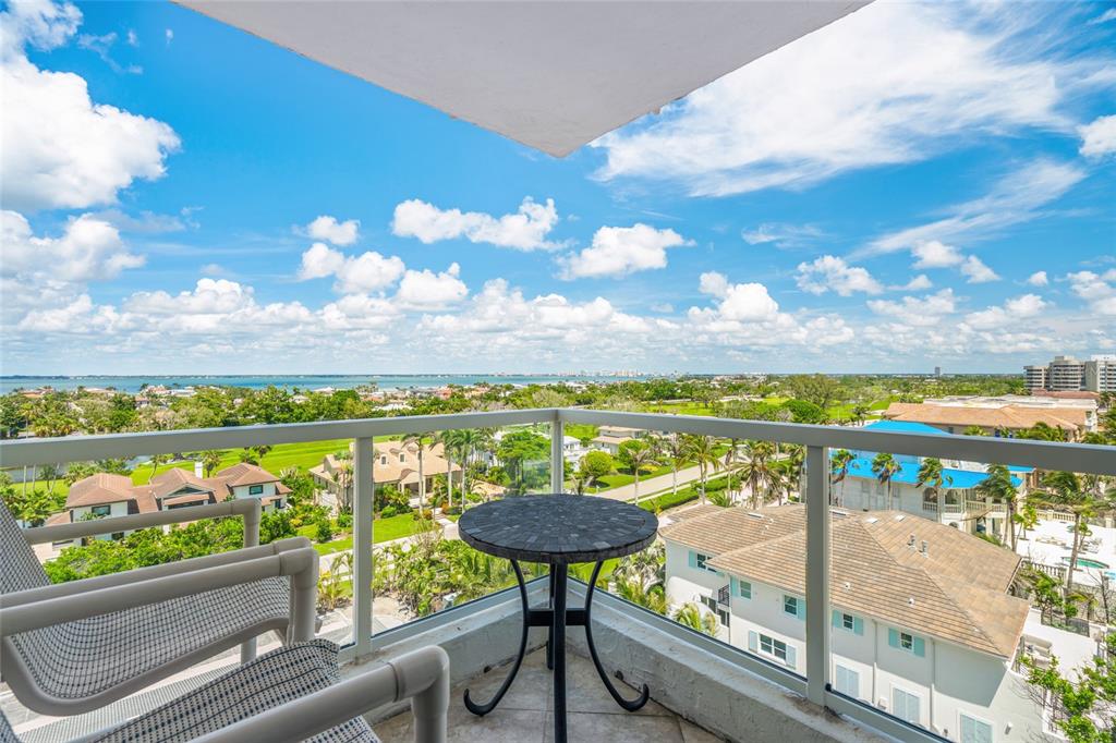 A balcony with a small table and chairs overlooks a residential neighborhood and the ocean — 1000 LONGBOAT CLUB ROAD, LONGBOAT KEY, FL