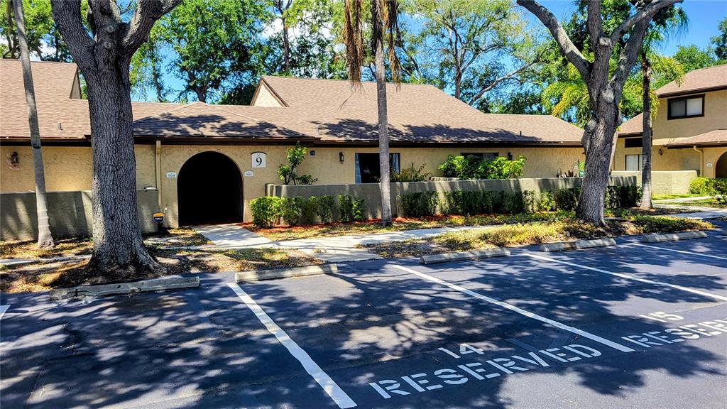 A tan, single-story residential building with a dark arched entryway and reserved parking spaces — 6262 142ND AVENUE N UNIT 905, CLEARWATER, FL