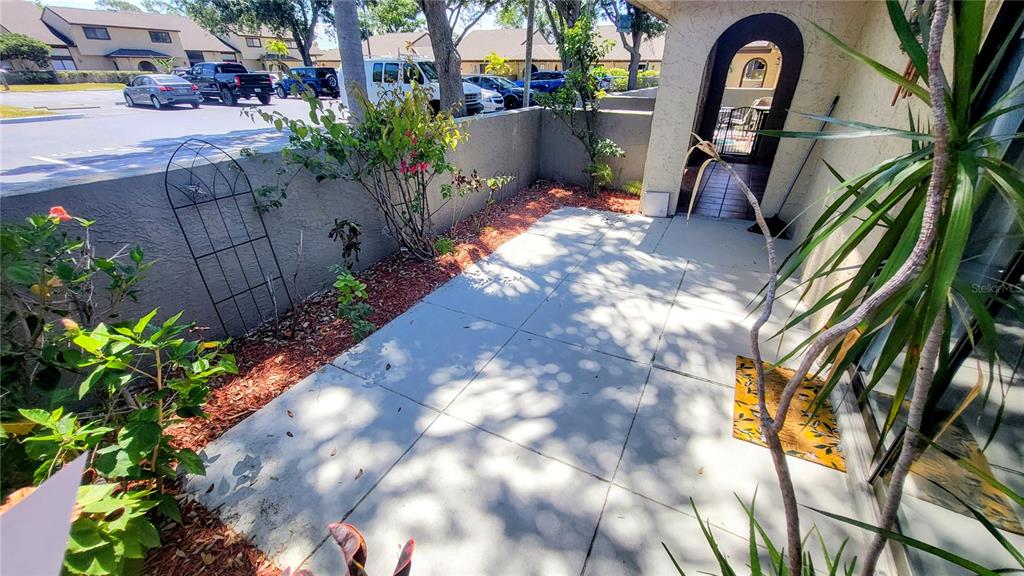 A concrete patio features a small garden bed, a metal trellis, and an arched entryway — 6262 142ND AVENUE N UNIT 905, CLEARWATER, FL