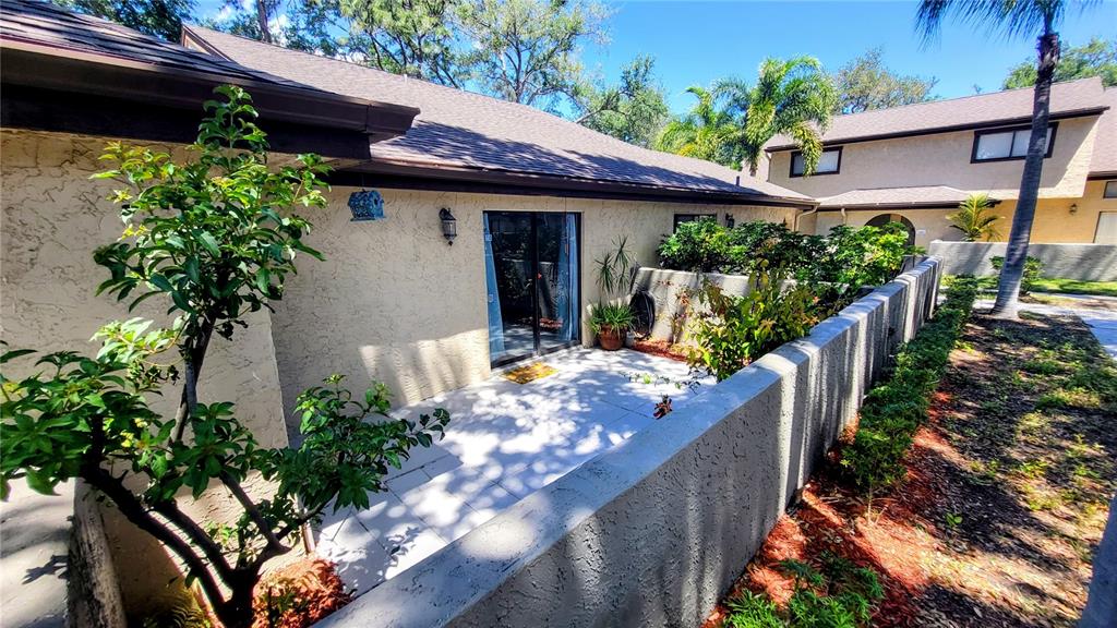 A patio with light-colored pavers is enclosed by a low wall next to a house — 6262 142ND AVENUE N UNIT 905, CLEARWATER, FL