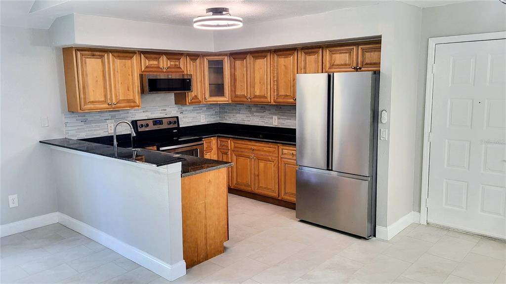 A kitchen features wood cabinets, black countertops, stainless steel appliances, and light-colored tile flooring — 6262 142ND AVENUE N UNIT 905, CLEARWATER, FL