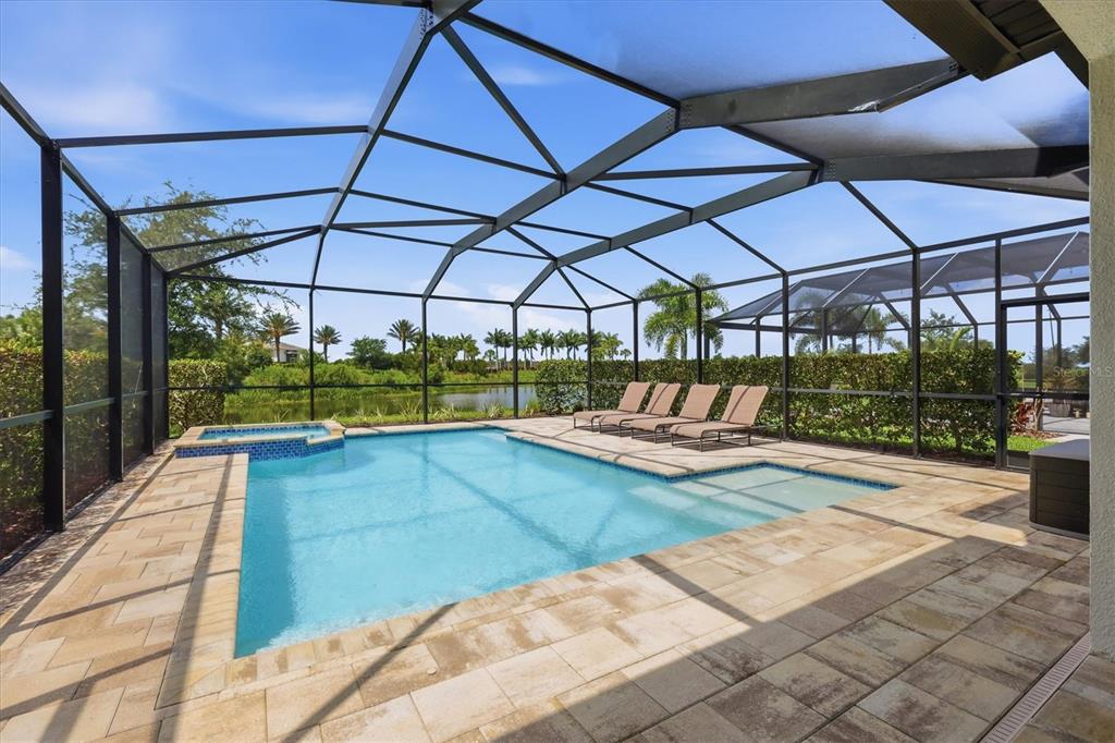 A screened-in pool area features a spa, lounge chairs, and a view of a pond — 8212 SHOOTING STAR RD, SARASOTA, FL