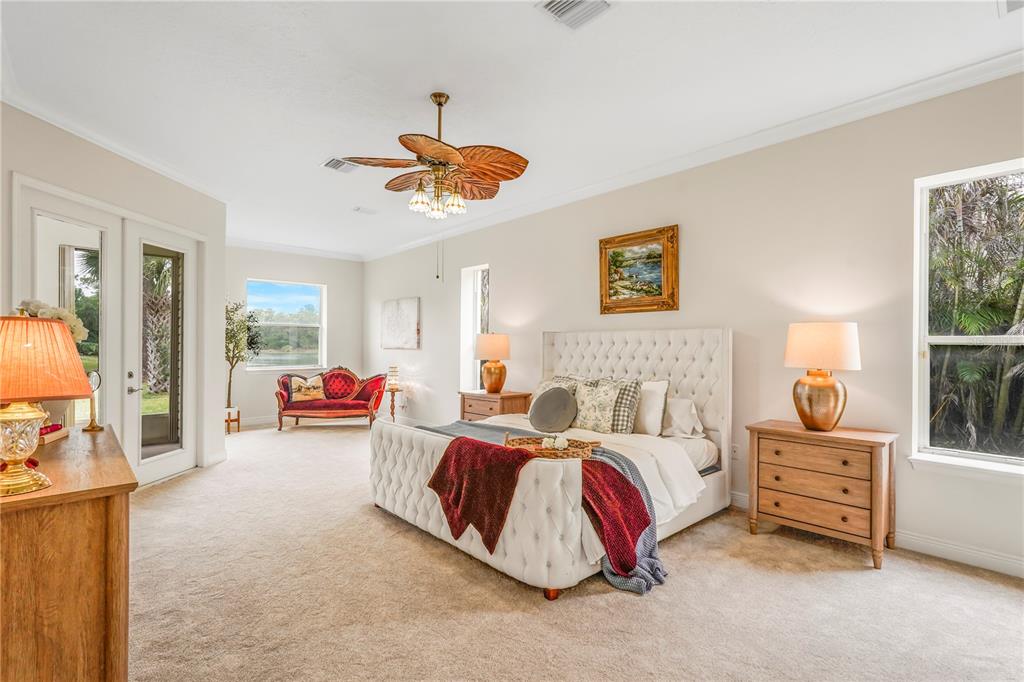 A spacious bedroom features a tufted white bed, a red settee, and a palm-leaf ceiling fan — 255 BRIGHTWATER DRIVE SE, PALM BAY, FL
