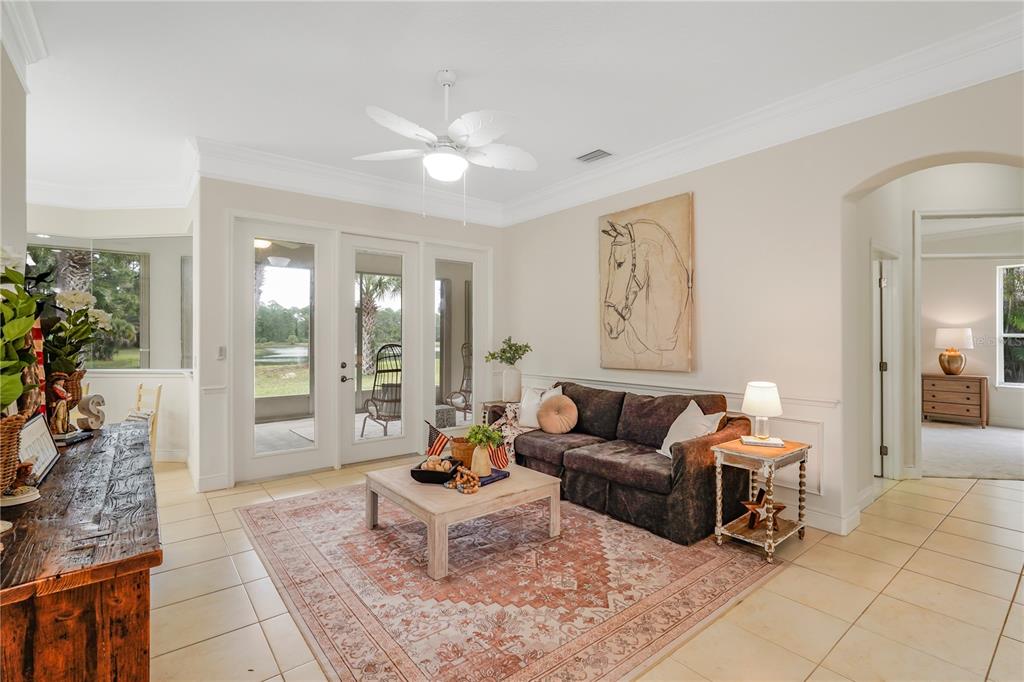 A living room features a brown sofa, a patterned rug, and glass doors overlooking a pond — 255 BRIGHTWATER DRIVE SE, PALM BAY, FL