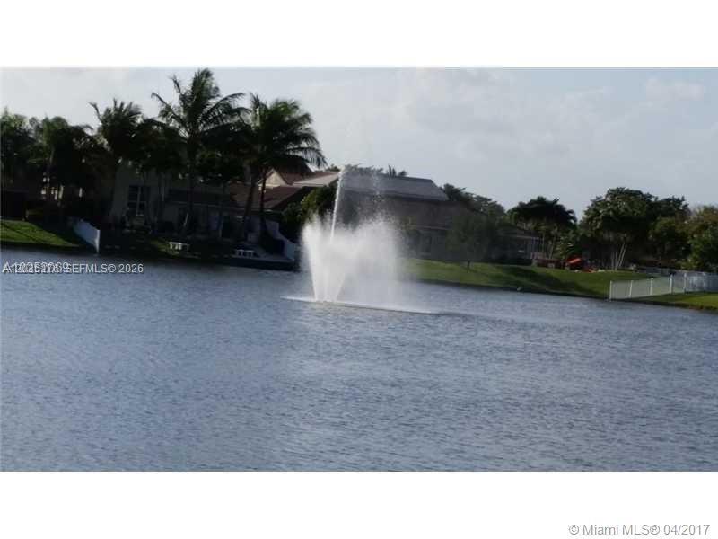 A water fountain sprays in the center of a lake surrounded by houses and trees — PLANTATION, FL