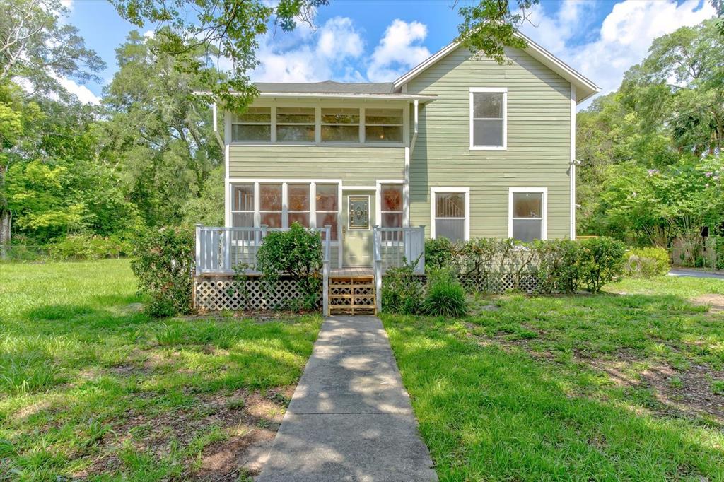 A two-story green house with a front porch, lattice skirting, and a concrete walkway — 543 N THORPE AVENUE, ORANGE CITY, FL