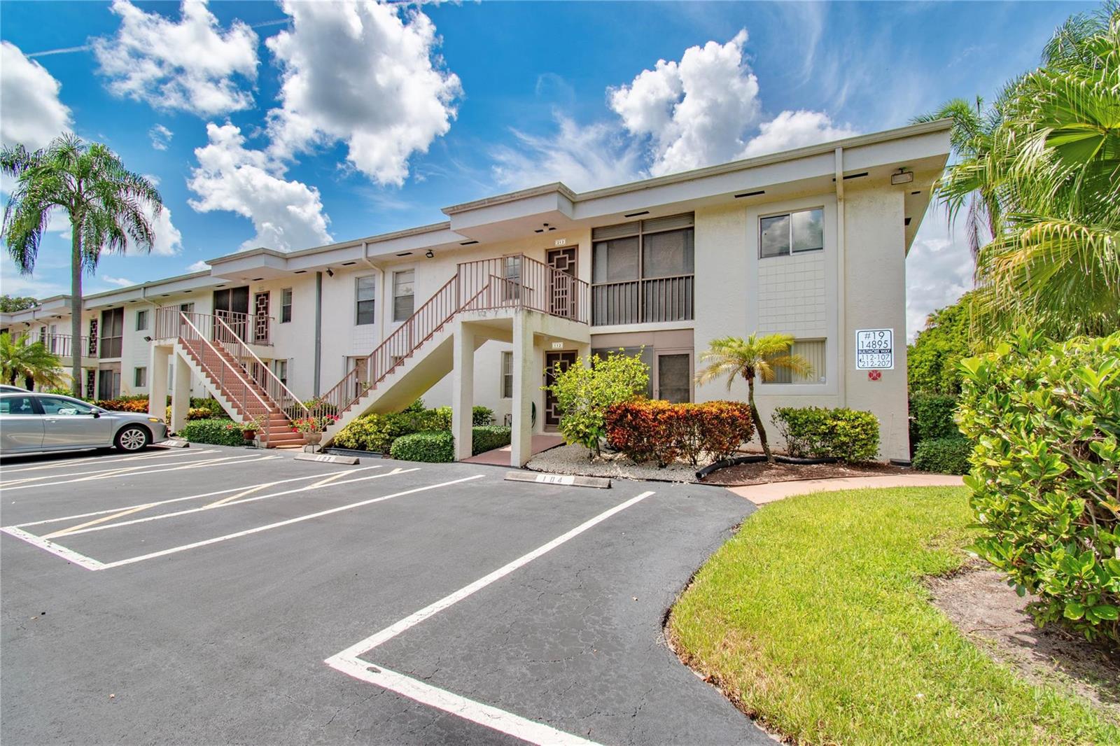 A two-story apartment building features exterior staircases, a parking lot, and tropical landscaping — 14895 Builtmore Way, Delray Beach FL 33446, DELRAY BEACH, FL