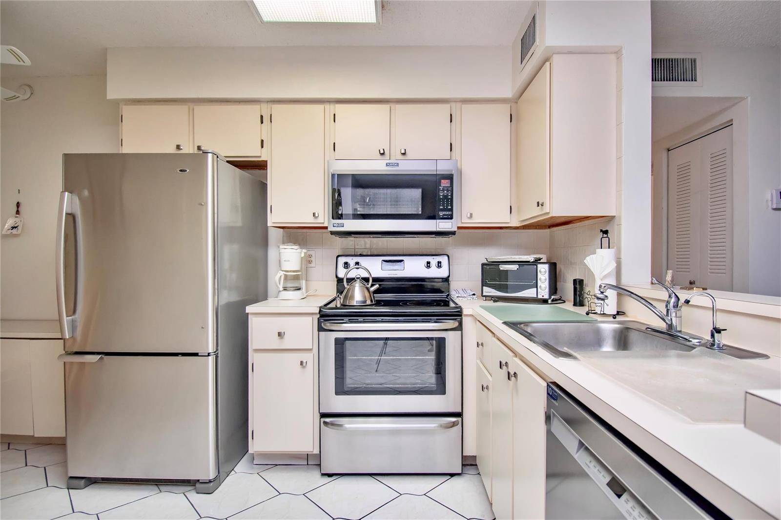 A kitchen with stainless steel appliances, off-white cabinetry, and white tiled flooring — 14895 Builtmore Way, Delray Beach FL 33446, DELRAY BEACH, FL
