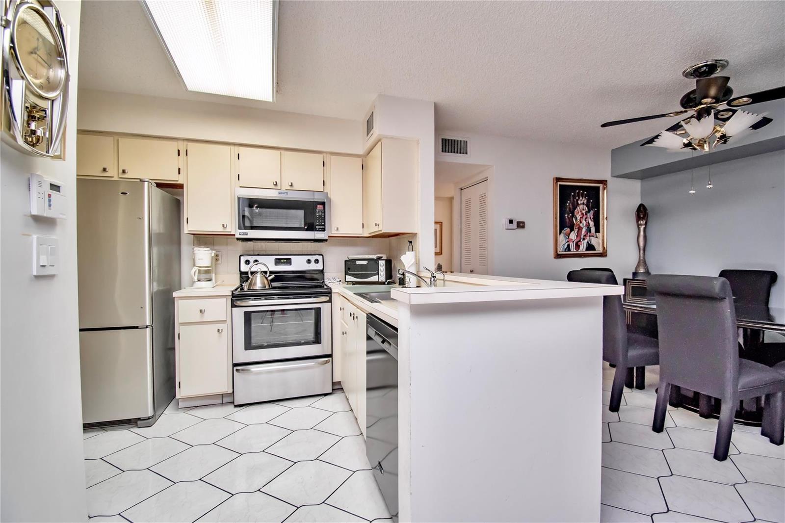 A kitchen with stainless steel appliances, off-white cabinets, and white tile flooring — 14895 Builtmore Way, Delray Beach FL 33446, DELRAY BEACH, FL