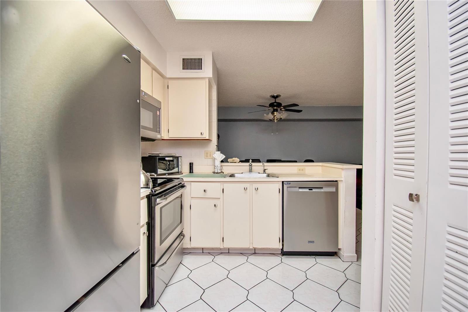 A kitchen features stainless steel appliances, white cabinets, and white tile flooring with dark grout — 14895 Builtmore Way, Delray Beach FL 33446, DELRAY BEACH, FL