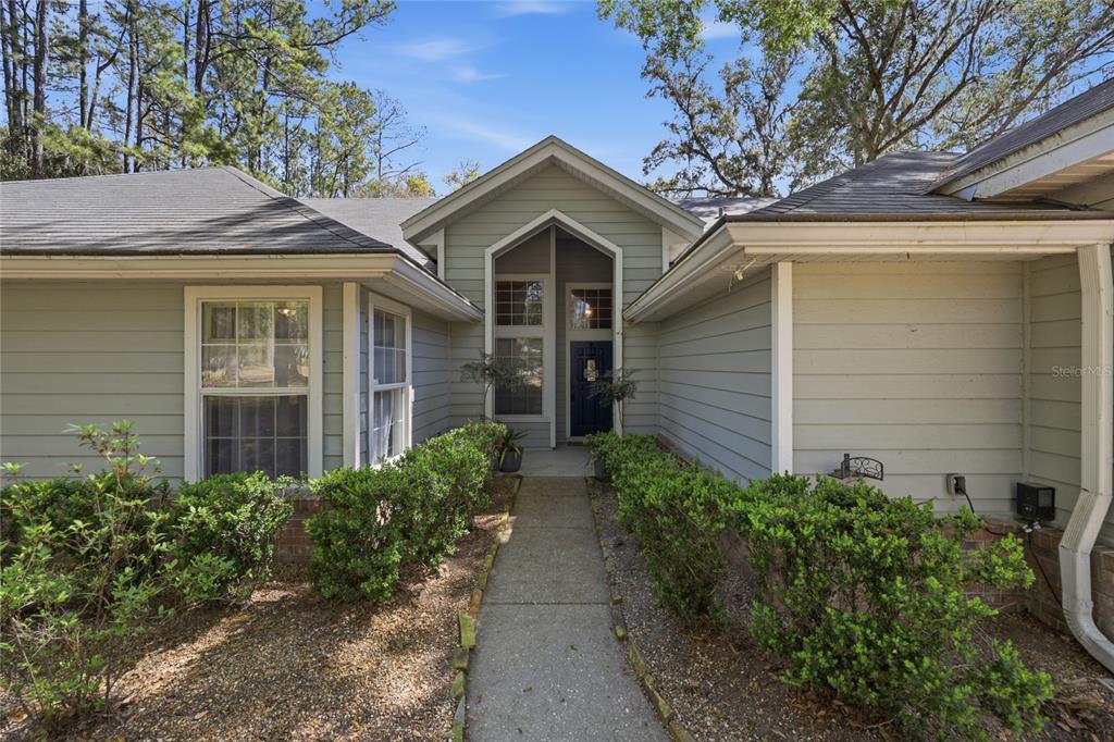 A light green house exterior features a gabled entryway, a concrete walkway, and landscaped bushes — 7615 NW 176TH STREET, ALACHUA, FL