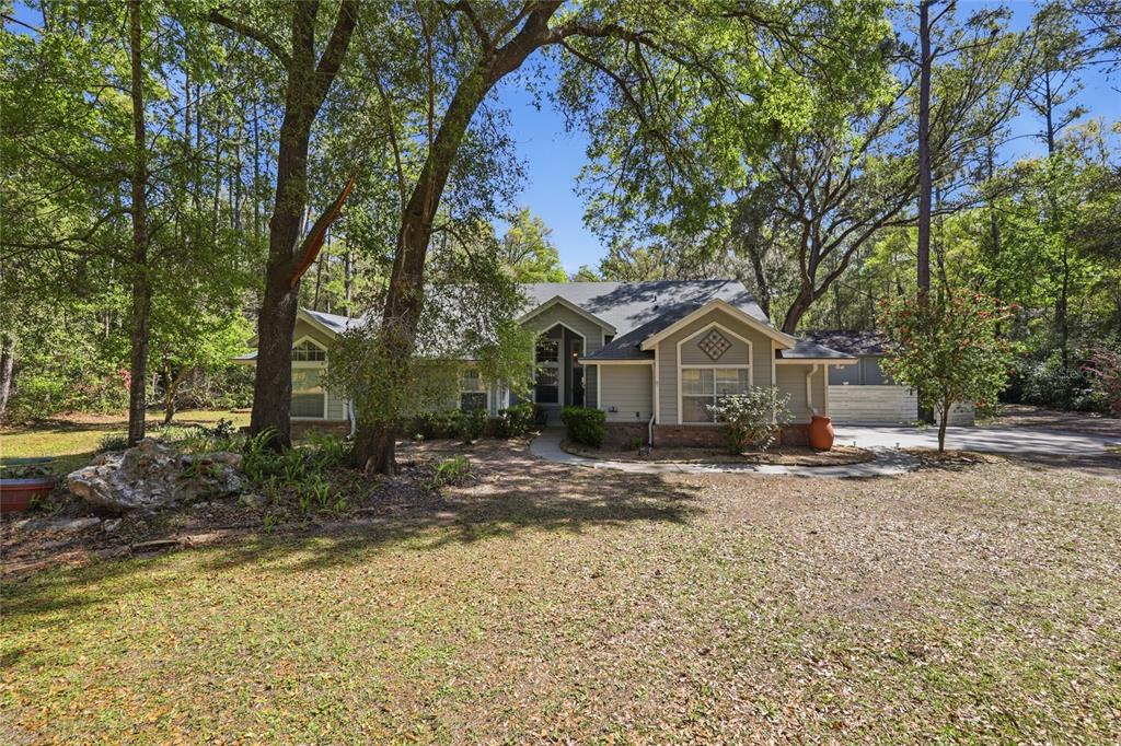 A single-story house with light green siding and a brick base sits among mature trees — 7615 NW 176TH STREET, ALACHUA, FL
