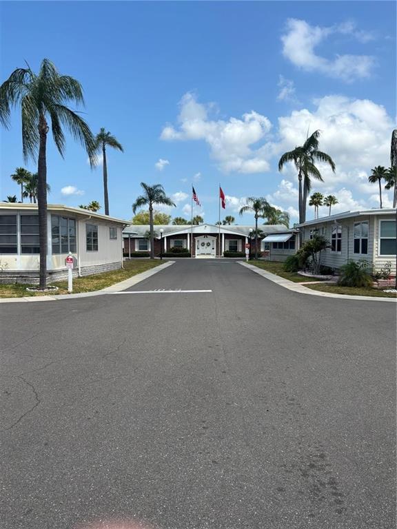 A paved road leads toward a community clubhouse flanked by palm trees and mobile homes — 7901 40TH AVENUE N UNIT 60, ST PETERSBURG, FL