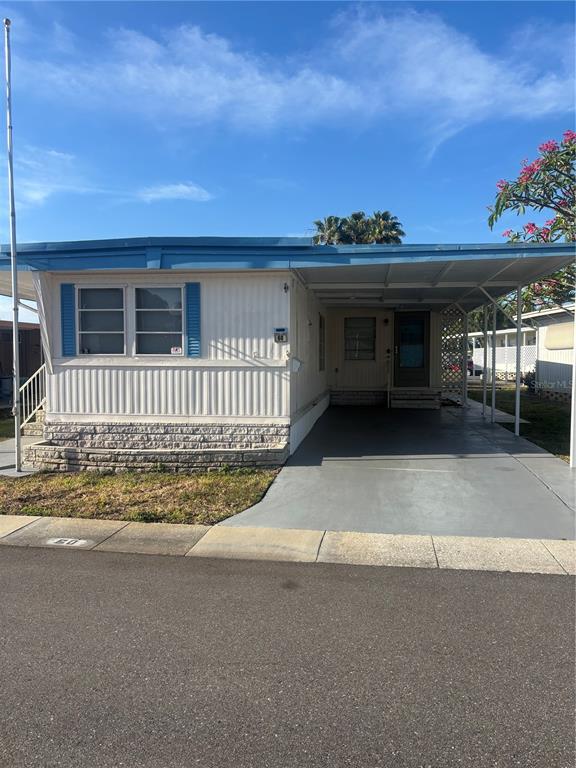 A single-story mobile home features white siding, blue shutters, and an attached carport — 7901 40TH AVENUE N UNIT 60, ST PETERSBURG, FL