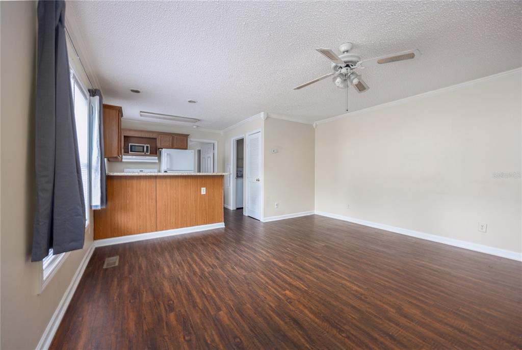 An open-concept living room with wood-look flooring, a ceiling fan, and an adjacent kitchen area — 2905 SW ARCHER ROAD UNIT S4024, GAINESVILLE, FL