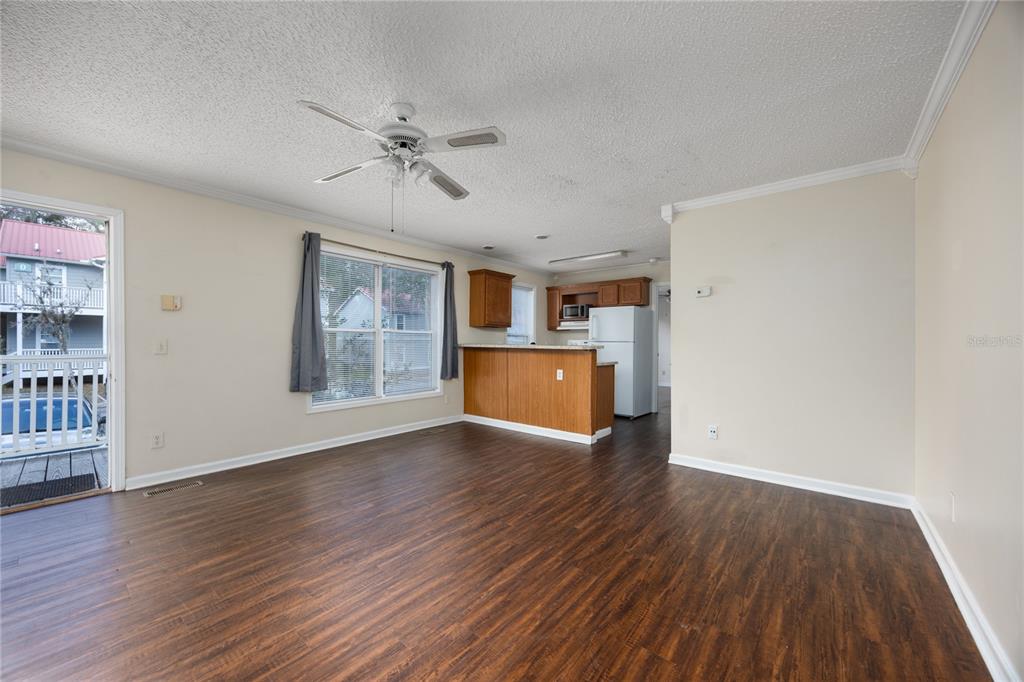 A living room with wood-look flooring, a ceiling fan, and an open kitchen with cabinets — 2905 SW ARCHER ROAD UNIT S4024, GAINESVILLE, FL
