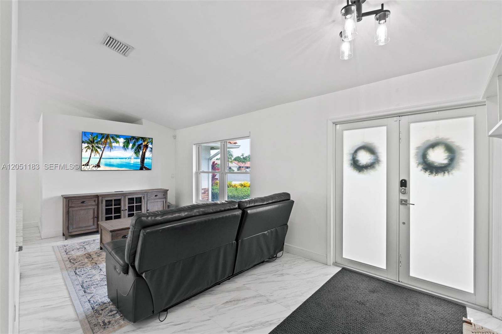A living room features a wall-mounted television, a dark leather sofa, and white flooring — 22433 Ensenada Way, Boca Raton FL 33433, BOCA RATON, FL